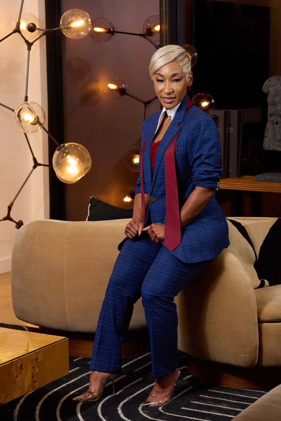 Cassandra G. Daniels in a blue windowpane suit with a burgundy tie, seated on the arm of a sofa.
